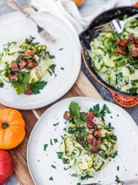 2 plates of cooked zucchini noodles with white sauce and tomatoes