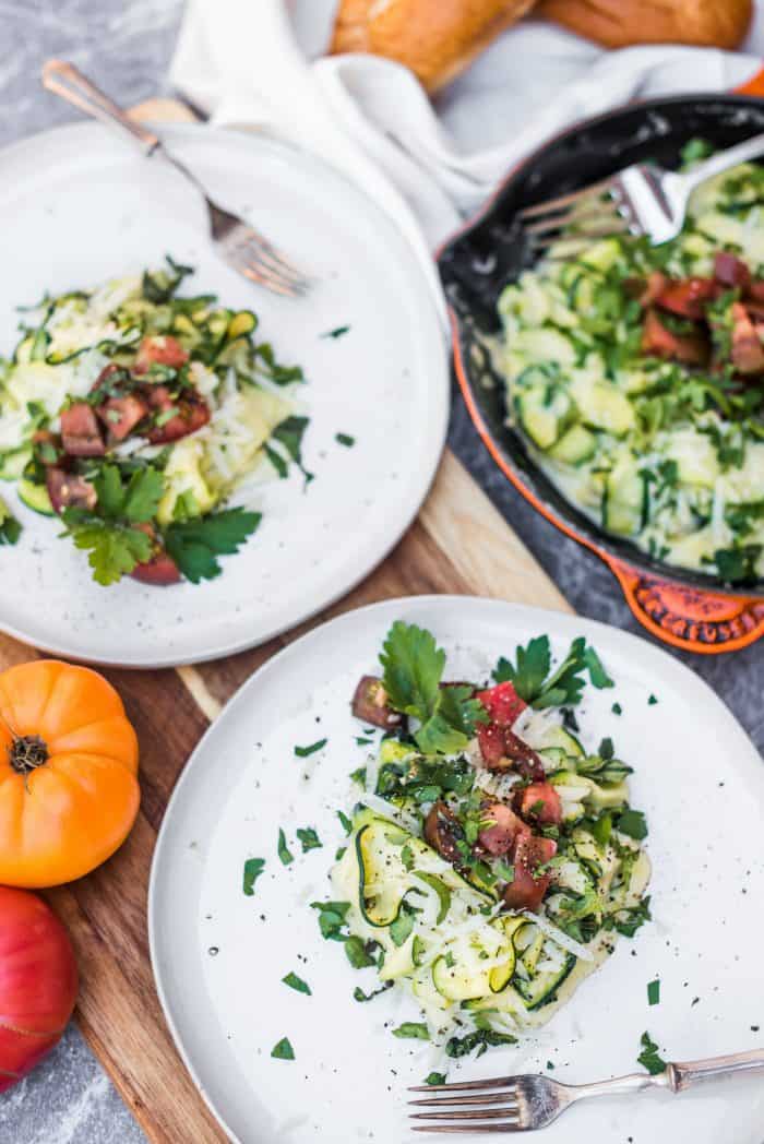 2 plates of cooked zucchini noodles with white sauce and tomatoes