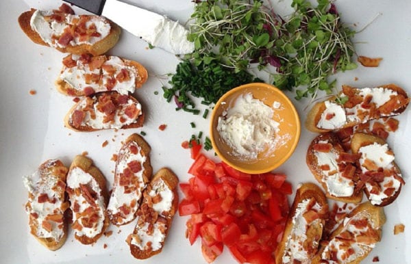 spreading goat cheese on crostini with bacon