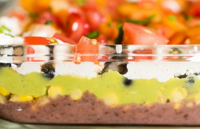close up 7 layer dip with beans, corn, guacamole, sour cream, olives, and tomatoes