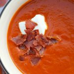 white bowl of tomato soup with creme fraiche and crunchy bacon on top