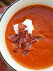 white bowl of tomato soup with creme fraiche and crunchy bacon on top