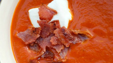 white bowl of tomato soup with creme fraiche and crunchy bacon on top