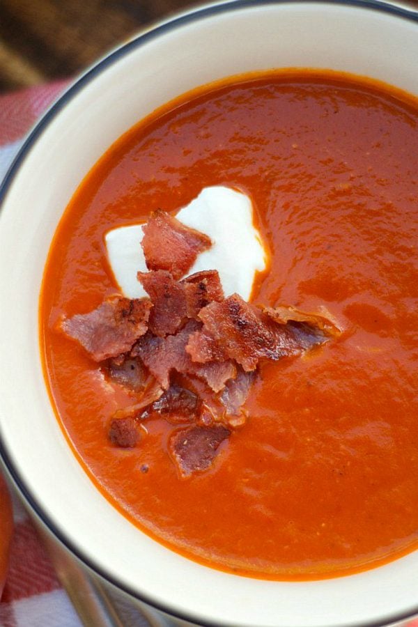 white bowl of tomato soup with creme fraiche and crunchy bacon on top