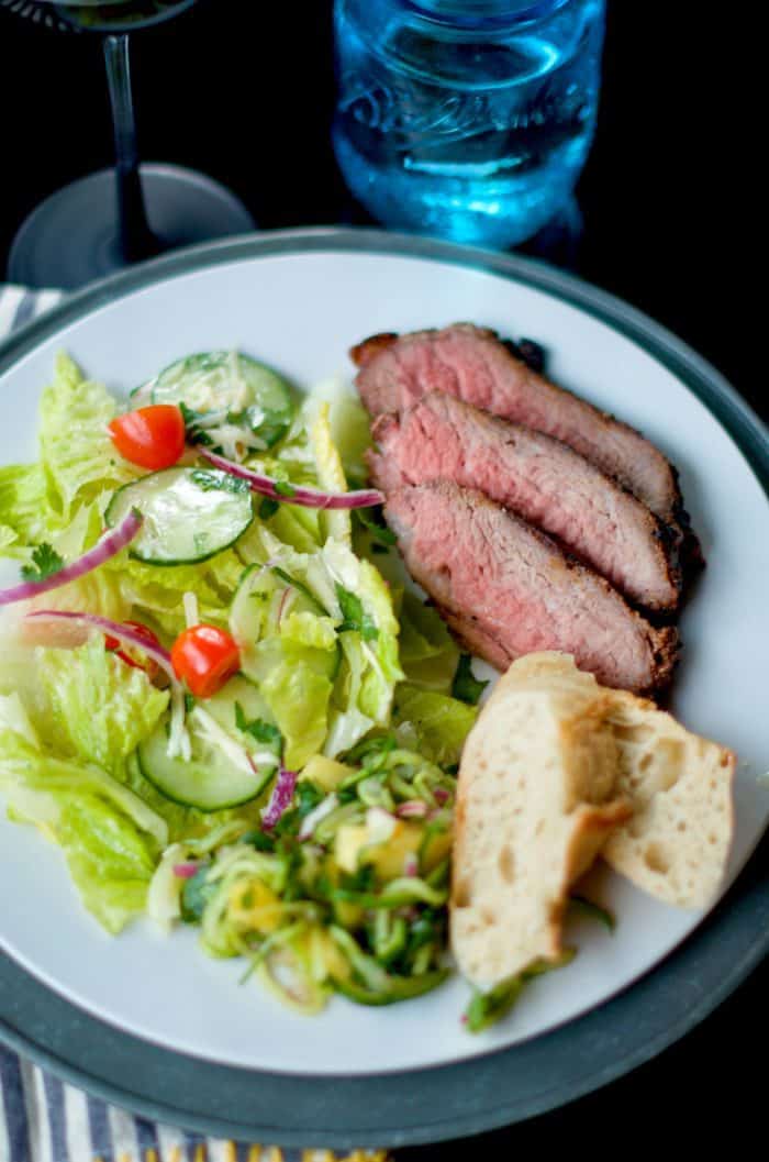 a white dinner plate with Grilled Garlic Pepper Tri Tip, salad, and bread