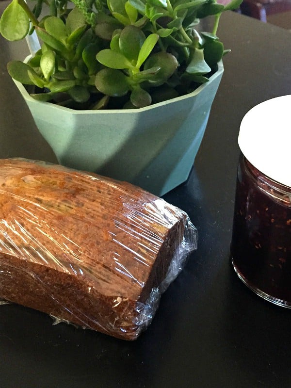 Sour Cream Banana Bread wrapped in plastic wrap with a jar of jam