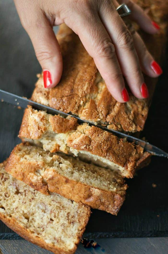 close up, hand slicing with knife a loaf of banana bread