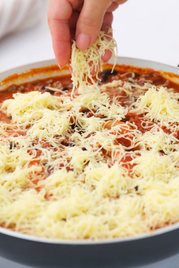 adding shredded cheese to Skillet Mexican Lasagna