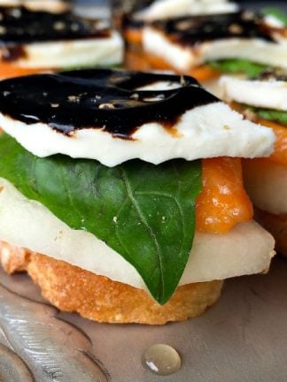 Persimmon Pear Caprese Crostini Appetizer: With creamy, fresh mozzarella, firm, sweet pears, and slices of persimmons, add a fresh basil leaf and serve on toasted crostini, drizzled with DeLallo's balsamic glaze!