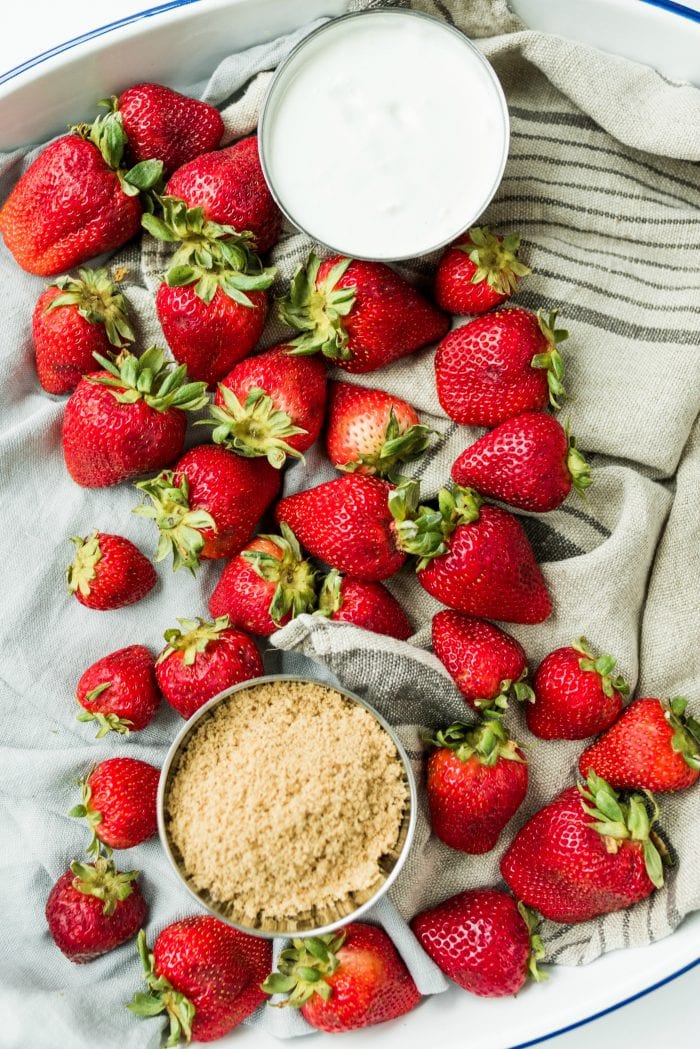 fresh strawberries on a linen towel with a bowl of sour cream and a bowl of dark brown sugar