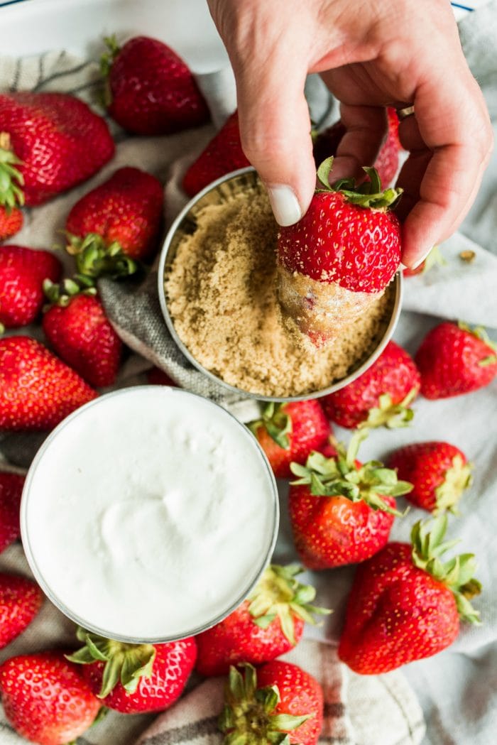 dipping a strawberry with sour cream on it, into a bowl of brown sugar