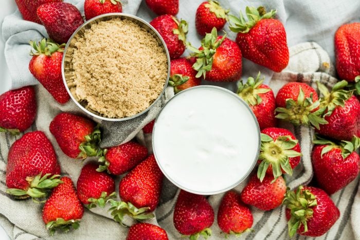 bowl of dark brown sugar and a bowl of sour cream, surrounded by fresh strawberries