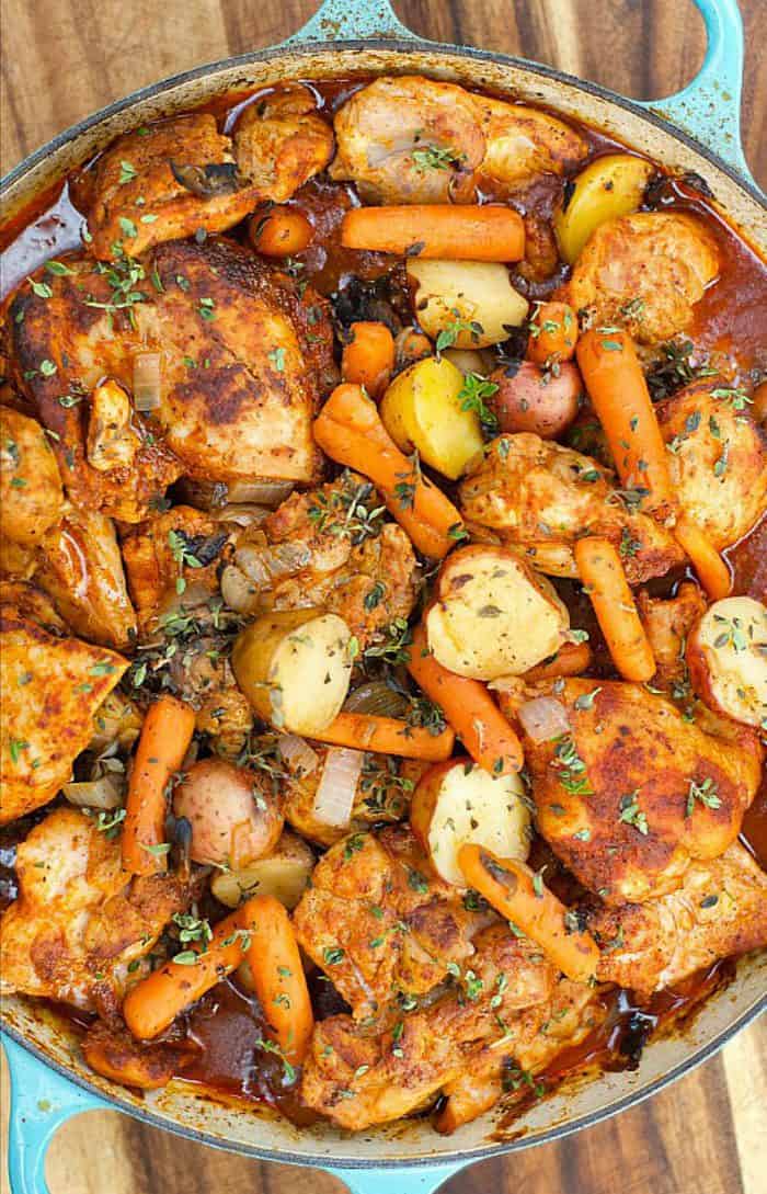 a blue braiser pan with paprika chicken thighs, carrots, and potatoes