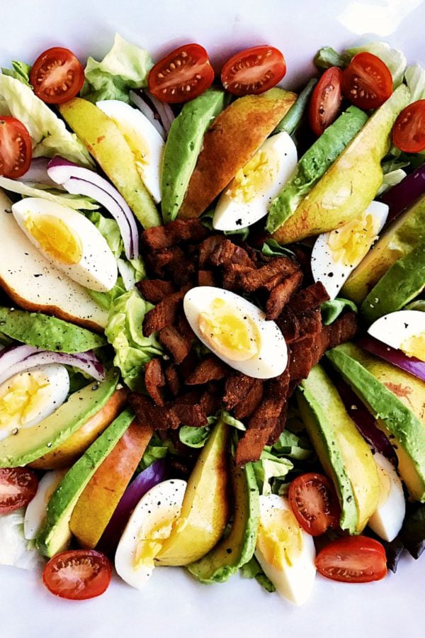 platter of sliced eggs, avocado, pear salad with crumbled bacon in the center