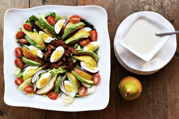 salad bowl of pear, bacon, avocado salad with blue cheese dressing on the side