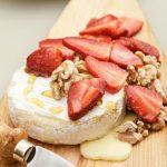 hot brie with fresh strawberries and toasted walnuts on top drizzled with honey