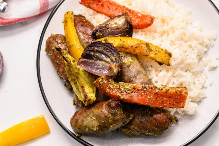 white plate with white rice, pesto brats, and peppers