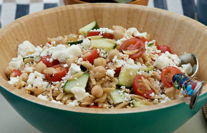 blue bamboo bowl filled with orzo salad with fresh tomatoes and feta cheese