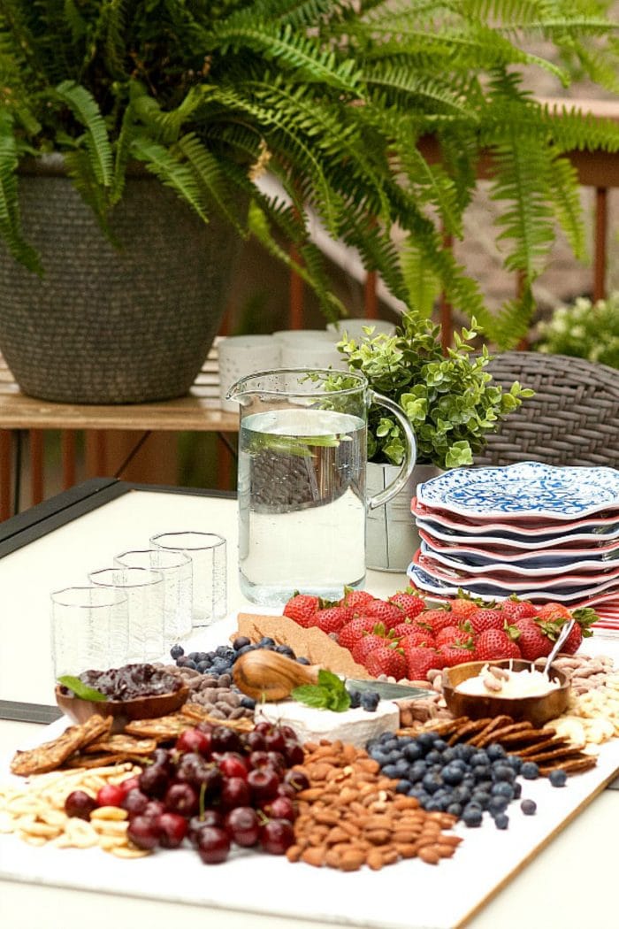 an outdoor setting with glasses, water pitcher, plates, and red, white and blue cheese board