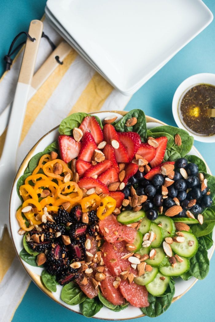 Summer Berry Almond Spinach Salad on a round platter with a small bowl of balsamic dressing