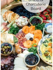 a breakfast spread with charcuterie meats, cheese, fruit, olive, and bowl of scrambled eggs