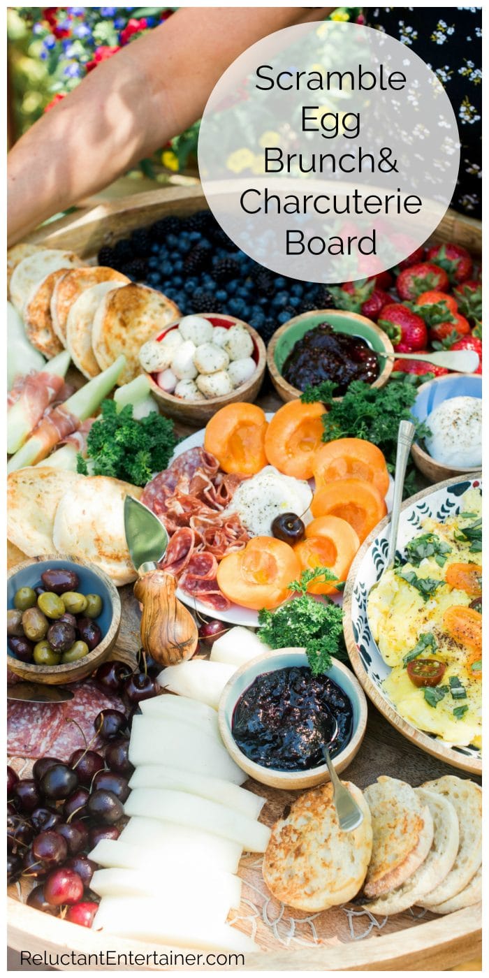 a breakfast spread with charcuterie meats, cheese, fruit, olive, and bowl of scrambled eggs