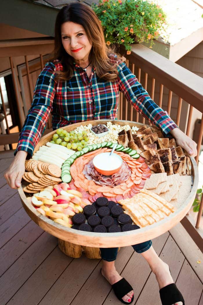 sitting down holidng a giant wood board filled with Grilled Cheese Sandwiches and Charcuterie Board foods