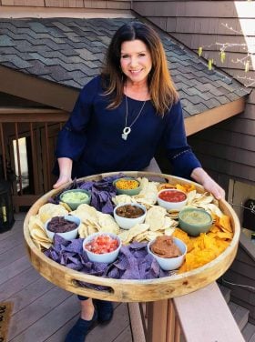 woman holing a large round board filled with chips and salsa