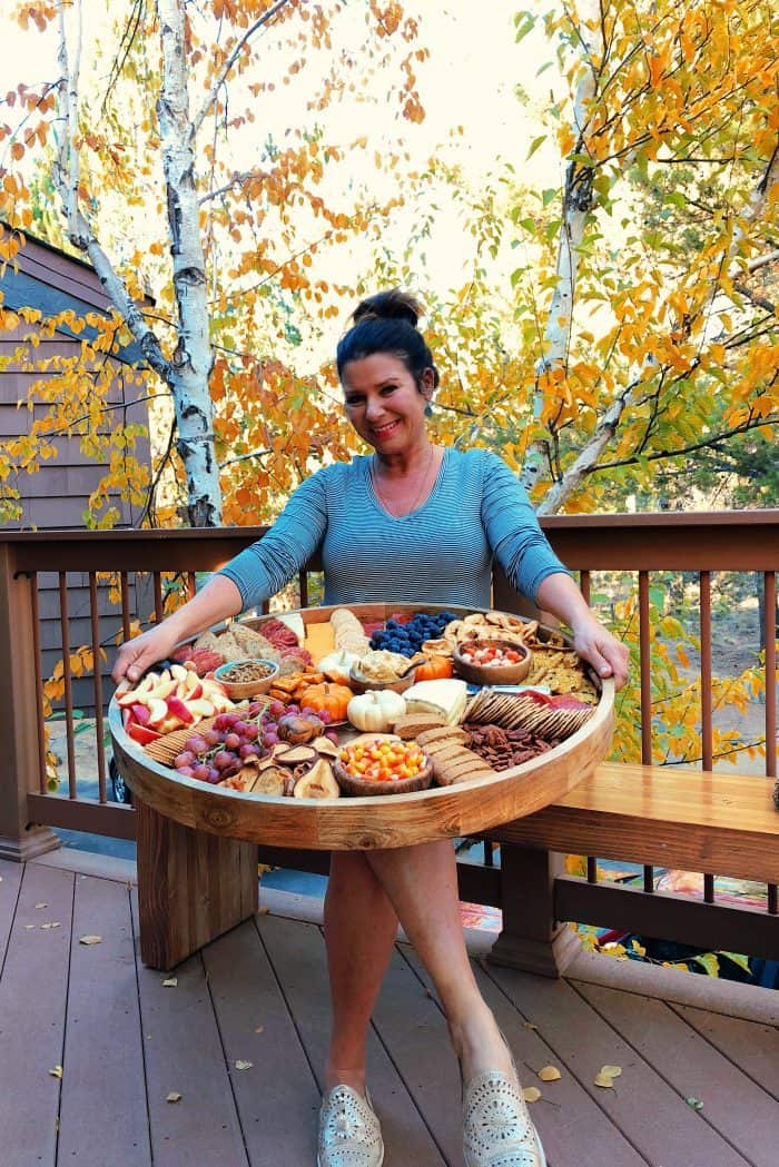 woman holding an Epic Charcuterie Board with fall colors in background