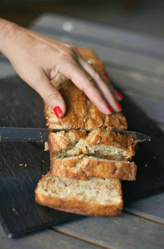 hand on top of Sour Cream Banana Bread loaf, slicing it with a knife