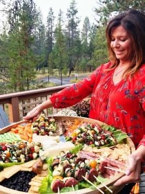 woman holding a big round wood board with appetizers