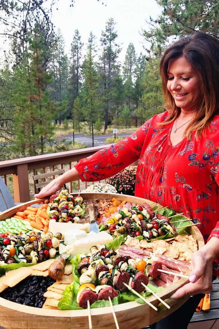 woman holding a big round wood board with appetizers