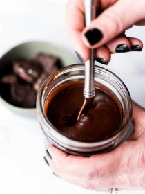 stirring homemade chocolate sauce in a pint size canning jar