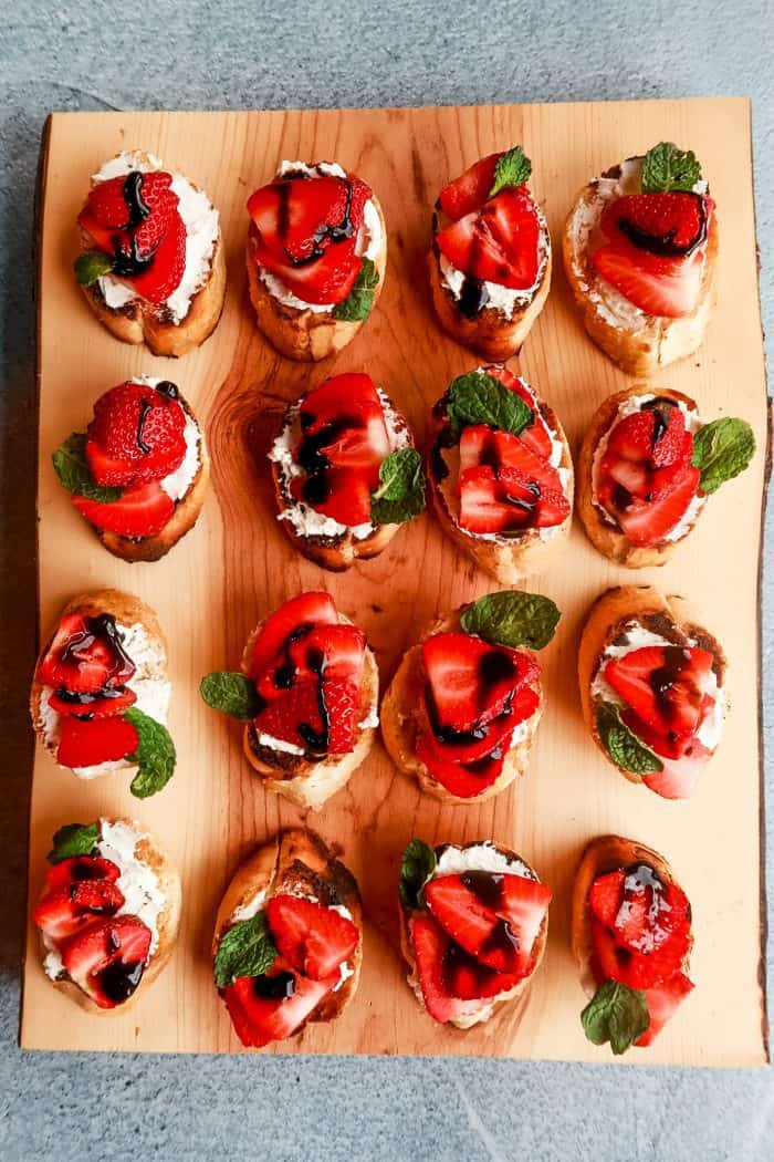 a wood board with 12 beautiful Strawberry Goat Cheese Bruschetta toasts