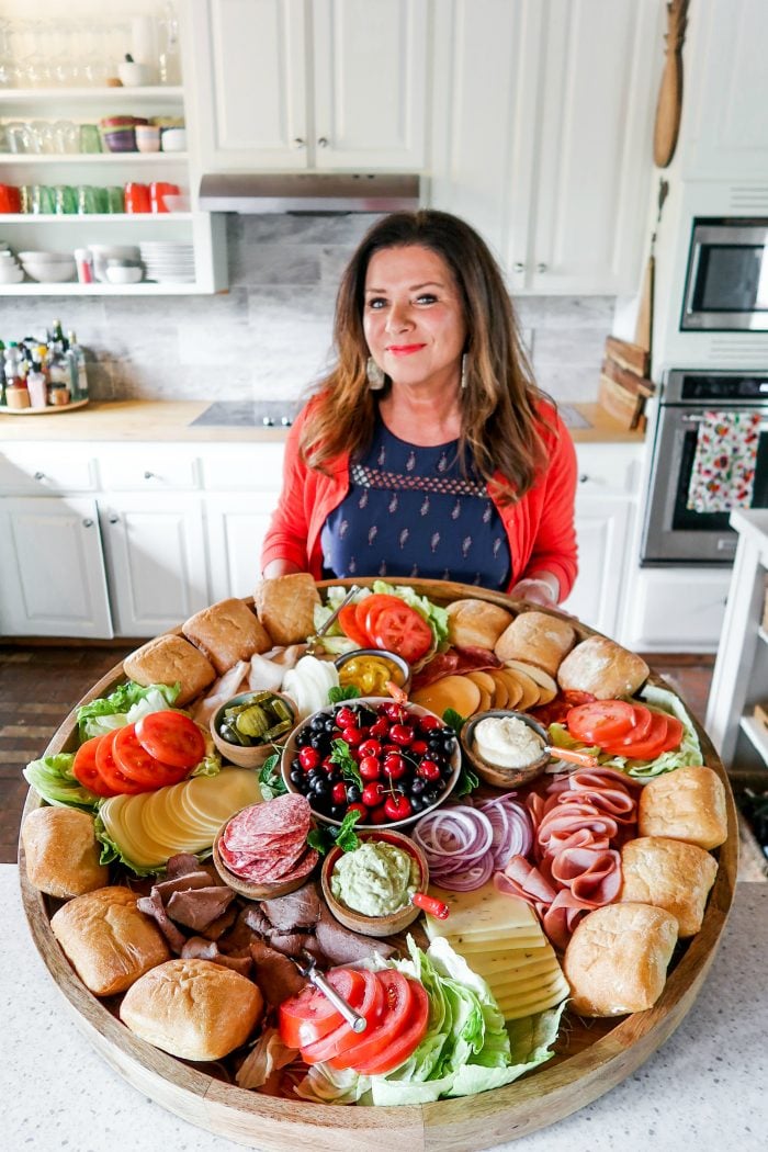 woman holidng a giant round board with deconstructed sandwich ingredients