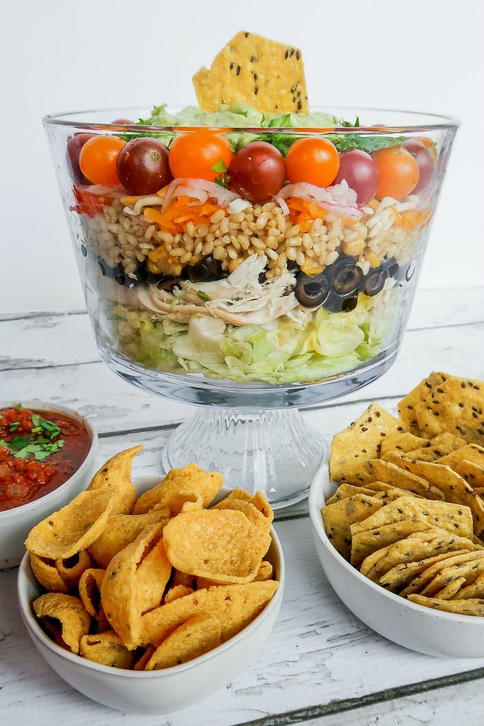 A chicken and rice salad with layers of tomatoes, olives, lettuce, in a glass bowl