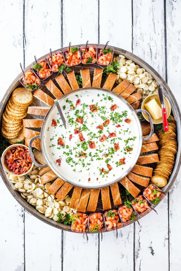 clam chowderin a big pot, on a round board with bread and shrimp cocktail cups