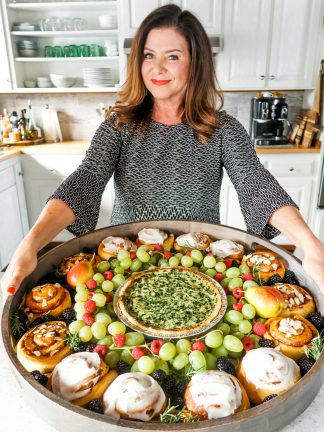 a woman holding a big board with quiche and cinnamon rolls