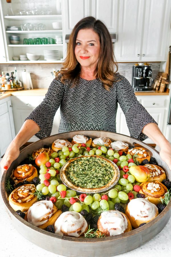 a woman holding a big board with quiche and cinnamon rolls