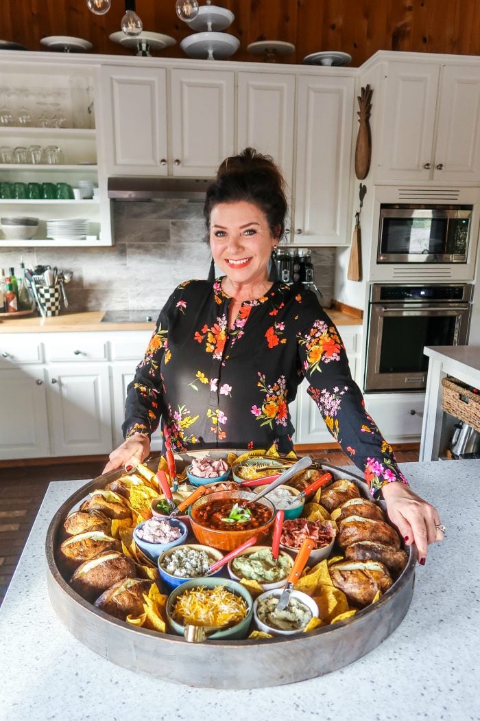 woman standing and holding a giant round board filled with potato bar ingredients