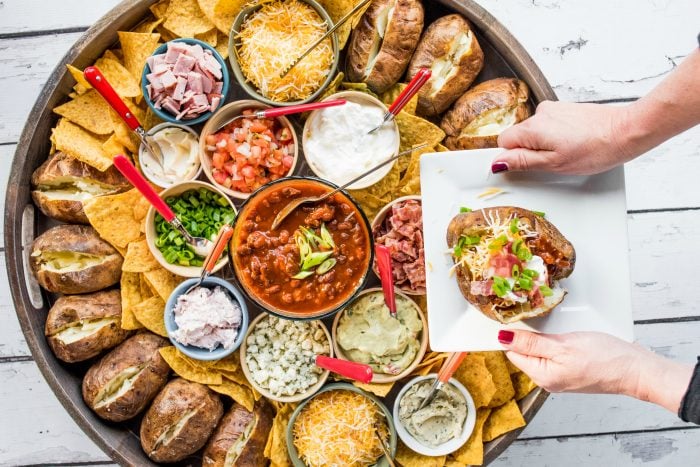 a woman's hands holidng a square plate with a stuffed baked potato