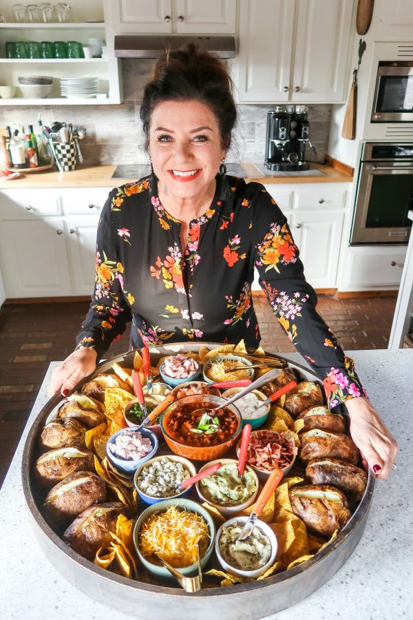 woman holding a round dinner board with baked potatoes and toppings