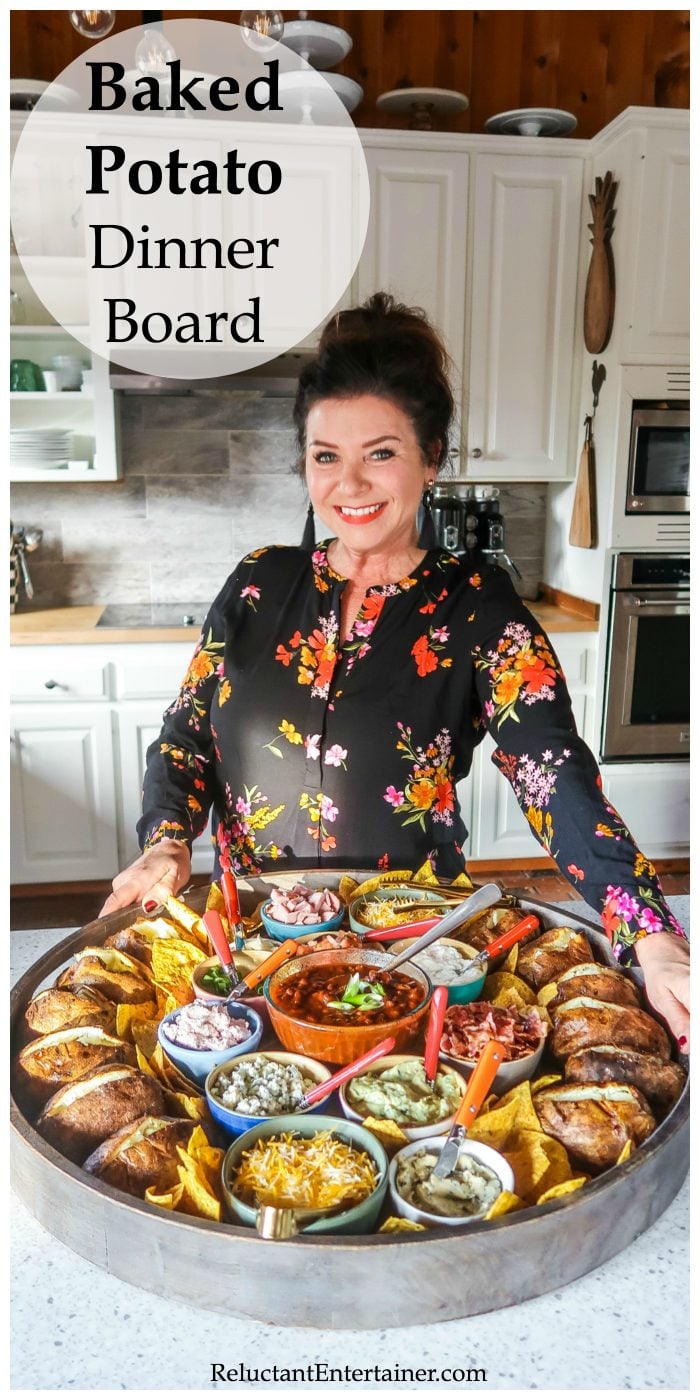 a woman holding a very large round board with 12 baked potatoes and bowls of toppings