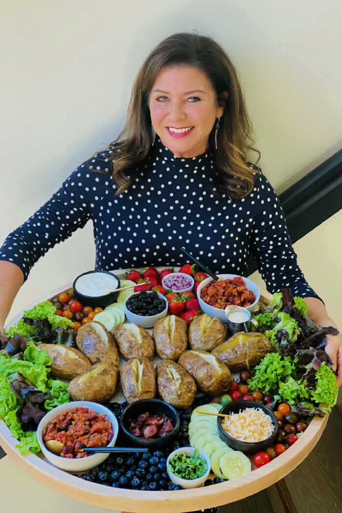 woman holding baked russet potatoes on potato board
