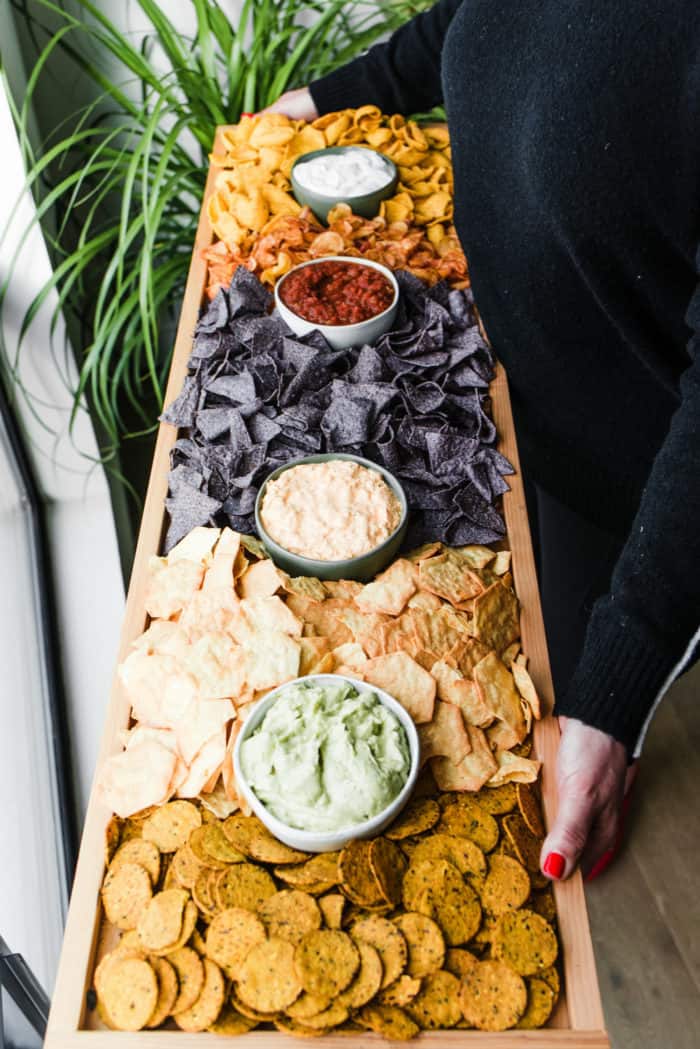 holding a long rectangular board filled with chips and dips (in small bowls)