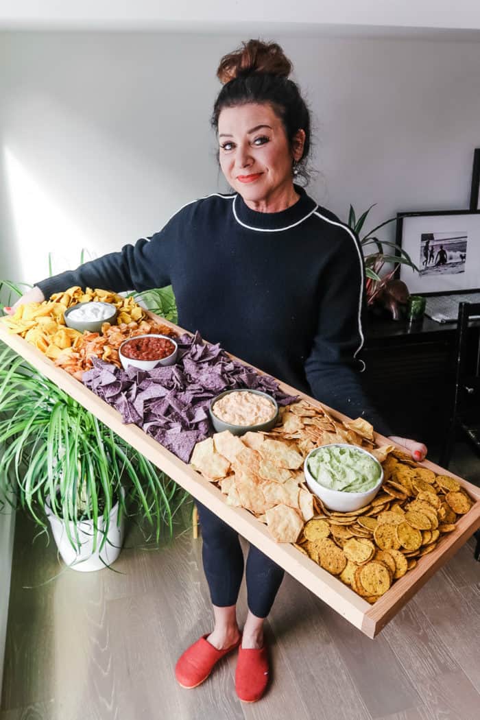 woman holding a 42 x 12 inch board filled with chips and dips
