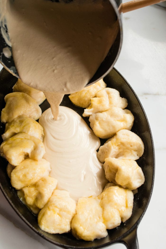 pouring melted cheese dip into dish lined with pretzel dough bites
