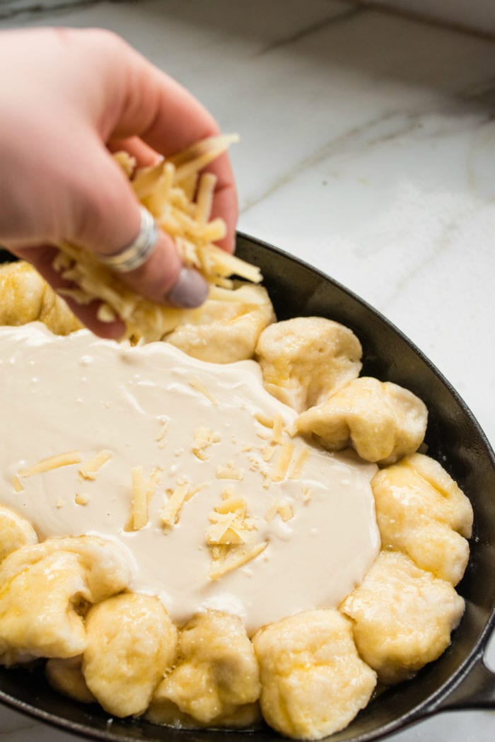 sprinkling shredded cheese on top of pretzel bites dish