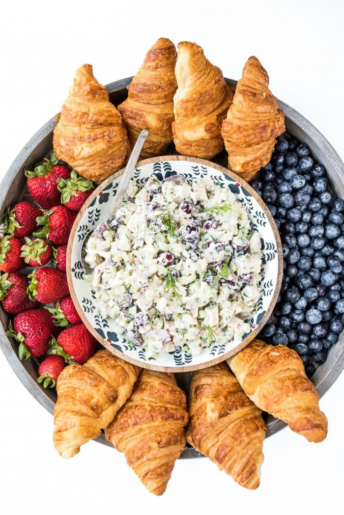 close up shot looking down on a wood board with chicken salad and croissants and fresh berries