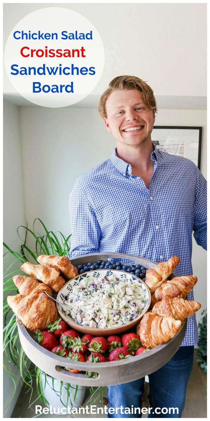 man holding a large wood board filled with chicken salad, croissants, and fresh berries